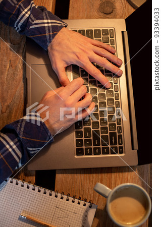 Young man drinking coffee in cafe and using laptop. Man's hands using laptop during coffee break Young man drinking coffee in cafe and using laptop. Man's hands using laptop during coffee break 93394033