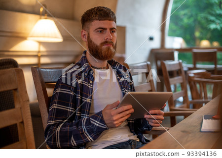 Freelancer dressed in casual outfit focus on reading news and looking on digital tablet while sitting in cozy urban cafe. Freelancer dressed in casual outfit focus on reading news and looking on digital tablet while sitting in cozy urban cafe. 93394136
