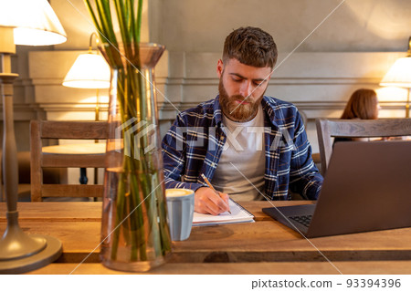 Casual business man or freelancer planning his work on notebook, working on laptop computer with smart phone, cup of coffee on table at coffee shop or home office. Casual business man or freelancer planning his work on notebook, working on laptop computer with smart phone, cup of coffee on table at coffee shop or home office. 93394396