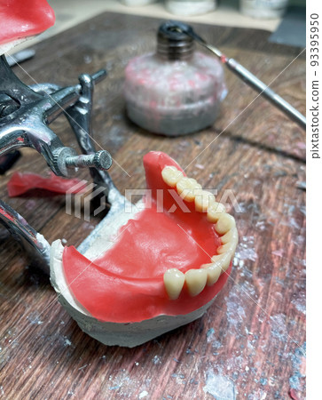 Artificial dentures in the manufacturing steps in the dental lab. Dental orthodontic mold with tools. Natural full prosthesis made of quality materials in plaster model. Selective focus, close up Artificial dentures in the manufacturing steps in the dental lab. Dental orthodontic mold with tools. Natural full prosthesis made of quality materials in plaster model. Selective focus, close up 93395950