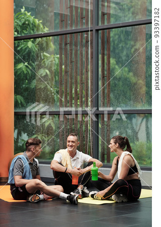 Positive young men and women drinking protein shakes when chatting after training in gym 93397182