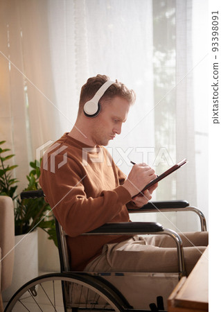 Creative young man in wheelchair listening to music in headphone when drawing on tablet computer 93398091