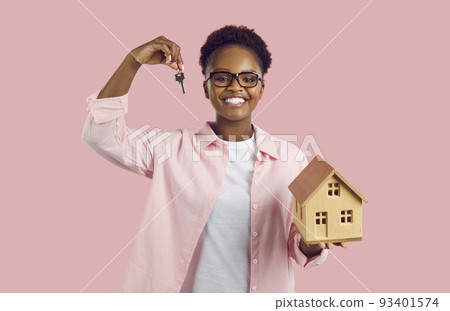 Portrait of joyful young African American woman with key and small wooden house in her hands. 93401574