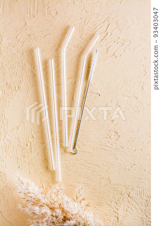 Glass reusable straws for drinks and cleaning brush on a beige textured background. Sustainable lifestyle. Top and vertical view. Glass reusable straws for drinks and cleaning brush on a beige textured background. Sustainable lifestyle. Top and vertical view. 93403047