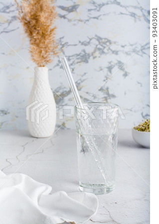 A glass of clean water and a glass straw for drinking on a light table. Diet organic lifestyle. Vertical view A glass of clean water and a glass straw for drinking on a light table. Diet organic lifestyle. Vertical view 93403091