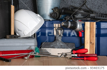 In celebration of Labor Day, a white protective construction helmet and a variety of construction tools are assembled on a wooden table. 93403175