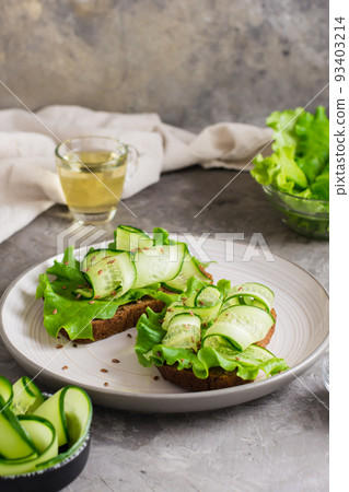 Appetizing bruschetta from rye bread, lettuce, cucumber and flax seeds on a plate on the table. Healthy diet food. Vertical view 93403214