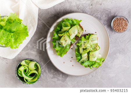 Ready-to-eat sandwiches with lettuce, cucumber and flax seeds on rye bread on a plate on the table. Healthy diet food. Top view 93403215