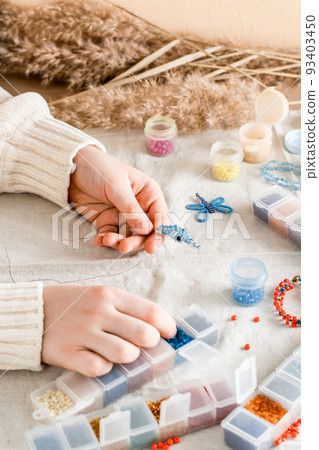 The girl's hands are weaving a dolphin on a table with items for beading. Development of creative skills and fine motor skills for children. Top and vertical view. 93403450