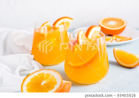 Hard seltzer carbonated orange cocktail with ice in glasses and orange slices on the table. Homemade drink. 93403816