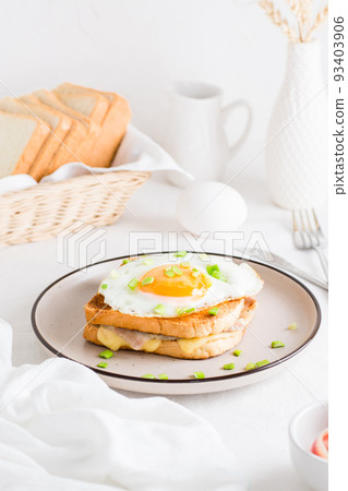 Croque madam sandwich with cheese, ham and egg on a plate on a light table. Hearty homemade breakfast. Vertical view 93403906