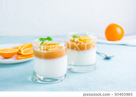 Panna cotta with orange and mint leaf in glasses on a light table. Sweet Italian dessert 93403965