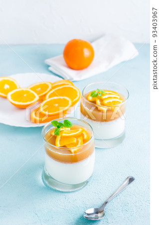 Orange panna cotta with mint leaf in glasses and orange slices on a plate on a light table. Sweet Italian dessert. Vertical view Orange panna cotta with mint leaf in glasses and orange slices on a plate on a light table. Sweet Italian dessert. Vertical view 93403967