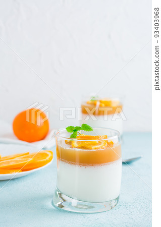 Panna cotta with orange and mint leaf in glasses on a light table. Sweet Italian dessert. Vertical view Panna cotta with orange and mint leaf in glasses on a light table. Sweet Italian dessert. Vertical view 93403968
