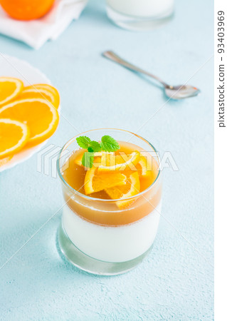 Homemade panna cotta with orange and mint leaf in a glass on a light table. Sweet Italian dessert. Vertical view. Close-up Homemade panna cotta with orange and mint leaf in a glass on a light table. Sweet Italian dessert. Vertical view. Close-up 93403969