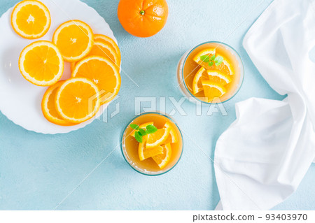 Panna cotta with orange and mint leaf in glasses on a light table. Sweet Italian dessert. Top view Panna cotta with orange and mint leaf in glasses on a light table. Sweet Italian dessert. Top view 93403970