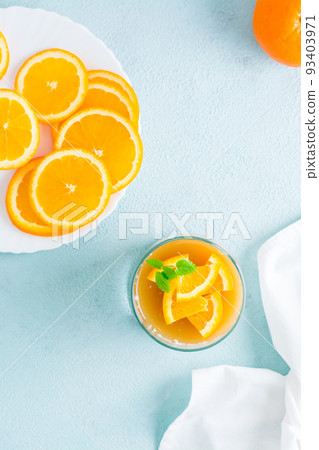 Orange panna cotta with mint leaf in glasses and orange slices on a plate on a light table. Sweet Italian dessert. Top and vertical view Orange panna cotta with mint leaf in glasses and orange slices on a plate on a light table. Sweet Italian dessert. Top and vertical view 93403971