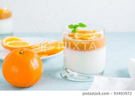 Homemade panna cotta with orange and mint leaf in a glass and a whole orange on a light table. Sweet Italian dessert Homemade panna cotta with orange and mint leaf in a glass and a whole orange on a light table. Sweet Italian dessert 93403972