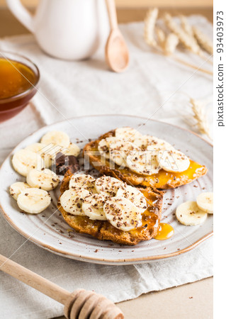 Ready to eat bruschettas with honey, banana and chocolate on a plate on the table. Vegetarian homemade snack. Vertical view Ready to eat bruschettas with honey, banana and chocolate on a plate on the table. Vegetarian homemade snack. Vertical view 93403973