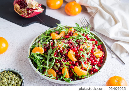 Fruit vitamin salad of pomegranate, tangerine, arugula and pumpkin seeds in a plate on the table. Organic vegetarian food. Fruit vitamin salad of pomegranate, tangerine, arugula and pumpkin seeds in a plate on the table. Organic vegetarian food. 93404013