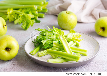 Sliced fresh celery stalk with leaves on a plate and green apples on the table ready to be cooked. Vegetarian food 93404030