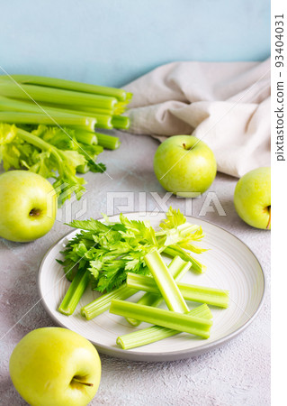 Sliced fresh celery stalk with leaves on a plate and green apples on the table ready to be cooked. Vegetarian food. Vertical view Sliced fresh celery stalk with leaves on a plate and green apples on the table ready to be cooked. Vegetarian food. Vertical view 93404031