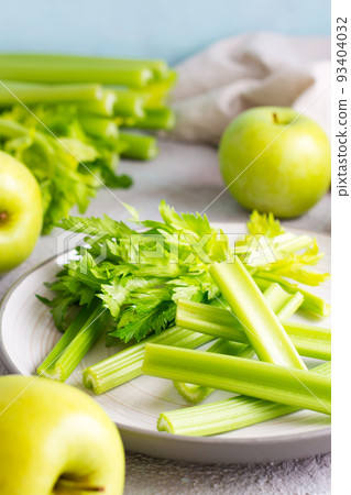 Sliced fresh celery stalk with leaves on a plate and green apples on the table ready to be cooked. Vegetarian food. Vertical view. Close-up 93404032