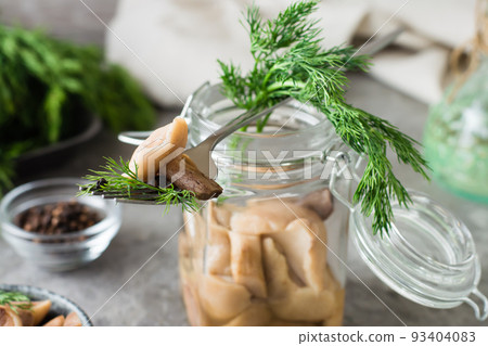 Pickled mushroom on a fork on a jar with boletus and dill and in a glass jar on the table. Vegetarian organic food. Close-up Pickled mushroom on a fork on a jar with boletus and dill and in a glass jar on the table. Vegetarian organic food. Close-up 93404083