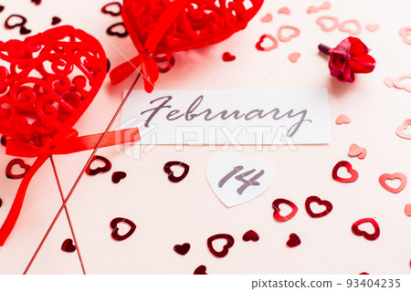 Valentine's Day. Date of February 14 and two curly red hearts on a pink background strewn with hearts. Close-up Valentine's Day. Date of February 14 and two curly red hearts on a pink background strewn with hearts. Close-up 93404235