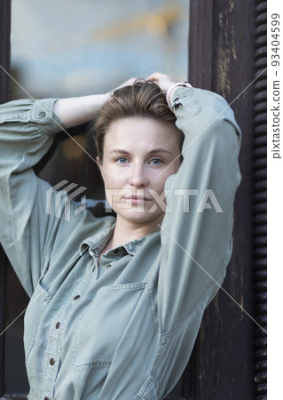 Sustainable, young smiling lovely European slav female blondie looks straighthood, old door is on background She keeps her hair up at the top, wears green - khaki denim Relaxed in summer day time. 93404599