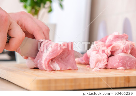 man cuts meat with knife on wooden board 93405229