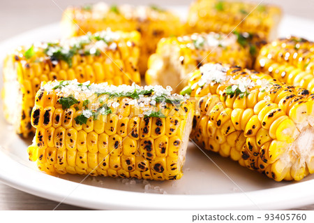 Corn grilled with salt and spices close up. Grilled corn on the cob with spices and sea salt on the whitel plate, close-up. 93405760