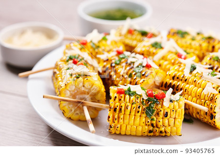 Chili and cheese grilled corn on cob, selective focus. Plate with grilled corn on cob sprinkled with cilantro and grated parmesan  on light background. 93405765