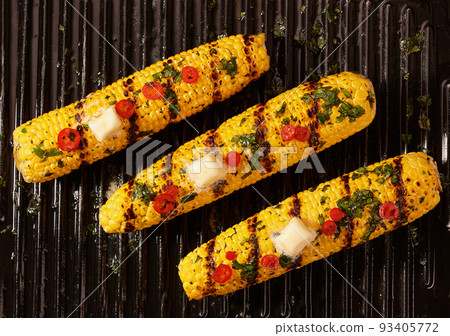grilled corn cob with melting butter and  chili pepper and cilantro, top view. Corn grilled with butter . 93405772