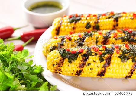 Plate with grilled corn on cob sprinkled with cilantro and chilli pepper on light background, selective focus. Plate with grilled corn on cob sprinkled with cilantro and chilli pepper on light background, selective focus. 93405775