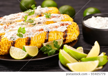 Roasted or grilled sweet corn cobs with with cream sauce, lime and cilantro, selective focus. Mexican street corn on dark table. Roasted or grilled sweet corn cobs with with cream sauce, lime and cilantro, selective focus. Mexican street corn on dark table. 93405779