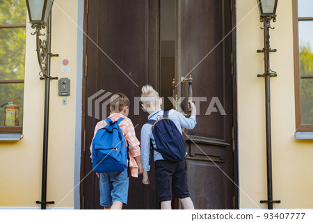 children entering school opening big wooden door. Boys with backpacks by school doorstep on sunny day. Begining of academic year. children entering school opening big wooden door. Boys with backpacks by school doorstep on sunny day. Begining of academic year. 93407777