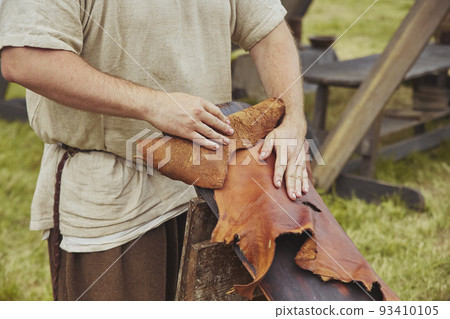 An artisan dressed in vintage clothing processes leather An artisan dressed in vintage clothing processes leather 93410105