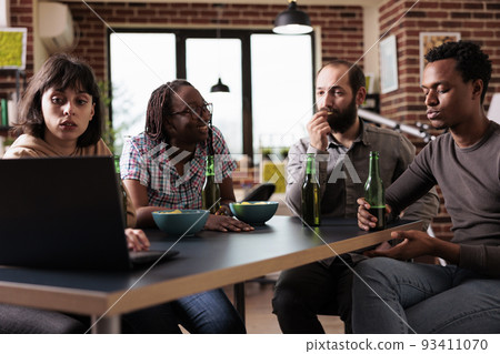Multiethnic group of friends sitting at home together while watching drama movies on laptop computer. Diverse people sitting at table in living room while enjoying leisure activity. 93411070