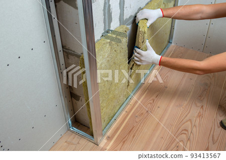 Worker insulating a room wall with mineral rock wool thermal insulation. 93413567
