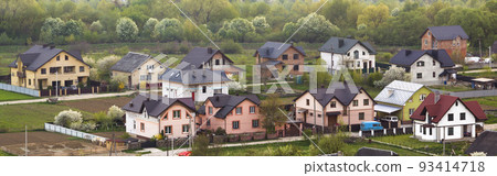 Quiet residential suburban area. Street with new modern comfortable brick cottages with yards and blooming gardens on background of beautiful green forest. Investments in real estate concept. Quiet residential suburban area. Street with new modern comfortable brick cottages with yards and blooming gardens on background of beautiful green forest. Investments in real estate concept. 93414718