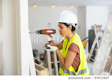 Asian woman repairer boring hole in wall with drill Asian woman repairer boring hole in wall with drill 93415687