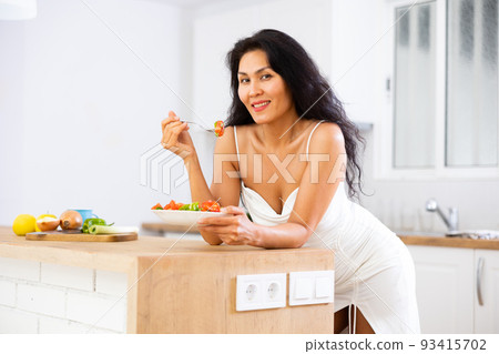 Portrait of woman eating salad at home 93415702