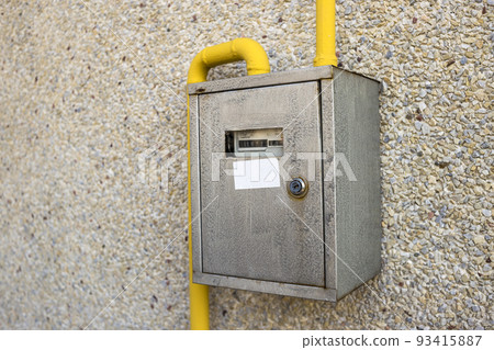 Close-up of metal steel gas meter box with connecting yellow pipes hanging on exterior light stone house wall. Construction, renovation, measurement tool and energy saving concept. 93415887