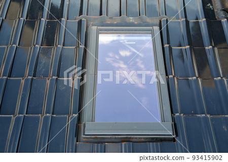 Closeup of attic window on house roof top covered with ceramic shingles. Tiled covering of building 93415902
