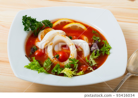 Spicy tomato soup with squids and greens in a white bowl 93416034
