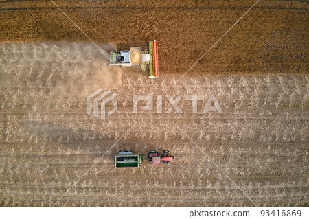 Aerial view of combine harvester and cargo trailer working during harvesting season on large ripe wheat field. Agriculture and transportation of raw grain concept Aerial view of combine harvester and cargo trailer working during harvesting season on large ripe wheat field. Agriculture and transportation of raw grain concept 93416869
