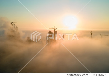 Aerial view of cement factory with high concrete plant structure and tower crane at industrial manufacturing site on foggy evening. Production and global industry concept. Aerial view of cement factory with high concrete plant structure and tower crane at industrial manufacturing site on foggy evening. Production and global industry concept. 93416876