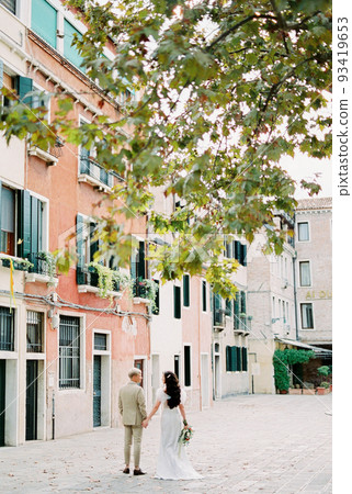 Bride and groom walking down an old street holding hands in Venice Bride and groom walking down an old street holding hands in Venice 93419653