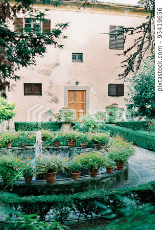 Fountain near an old villa surrounded by blooming flower pots Fountain near an old villa surrounded by blooming flower pots 93419656